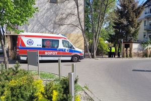 Na zdjęciu z lewej strony budynek, przed którym znajduje się karetka, a po prawej widoczni umundurowani policjanci którzy stoją na podwórku