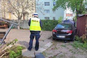 Umundurowany policjant przeprowadza oględziny pojazdu zaparkowanego na podwórku