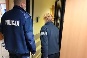 Umundurowany policjant wprowadza zatrzymaną kobietę do pomieszczenia dla osób zatrzymanych