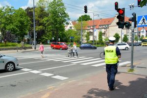 Umundurowany policjant stoi przy skrzyżowaniu i obserwuje osoby idące po przejściu dla pieszych