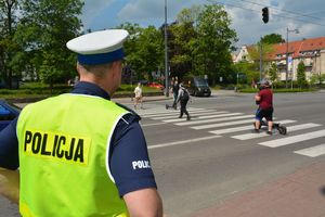 Umundurowany policjant stoi przy skrzyżowaniu i obserwuje osoby idące po przejściu dla pieszych