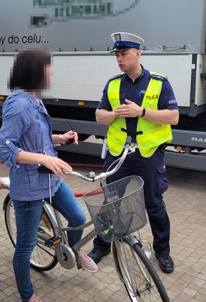 Umundurowany policjant rozmawia z rowerzystką. Za nimi naczepa samochodu ciężarowego