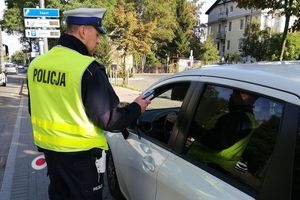 Umundurowany policjant stoi przy samochodzie. W samochodzie siedzi kierujący. Zdjęcie archiwalne