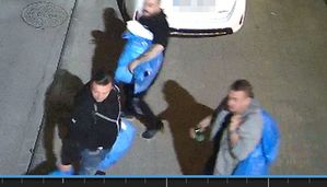 Trzech mężczyzn trzyma torby i stoi na drodze. Za nimi w tle fragment białego samochodu.