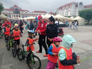 Policjantka i ratownik wodny na placu rozdają dzieciom na rowerach opaski.