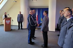 Pomieszczenie służbowe. Komendant Wojewódzki Policji w Gdańsku i Komendant Miejski Policji w Sopocie gratulują umundurowanemu policjantowi. Z prawej strony stoją umundurowani policjanci. W tle przy mównicy stoi kobieta w stroju cywilnym, a obok umundurowany policjant.