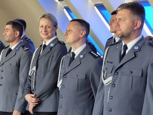 Umundurowani policjanci stoją w rzędzie. Policjantka stojąca w tym rzędzie uśmiecha się.