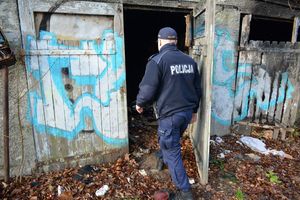 Pora jesienno-zimowa. Umundurowany policjant wchodzi do opuszczonego garażu - zdjęcie archiwalne.