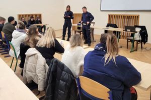 Aula. Umundurowani policjanci rozmawiają z młodymi osobami, które siedzą przy ławkach.