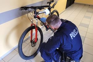 Umunduorwany policjant przeprowadza oględziny roweru, który stoi na korytarzu. Zdjęcie archiwalne.