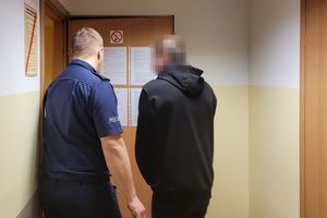 Umundurowany policjant wprowadza do pokoju mężczyznę w stroju cywilnym
