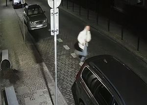 Pora nocna. Mężczyzna ucieka przez ulicę, na której stoją zaparkowane samochody.