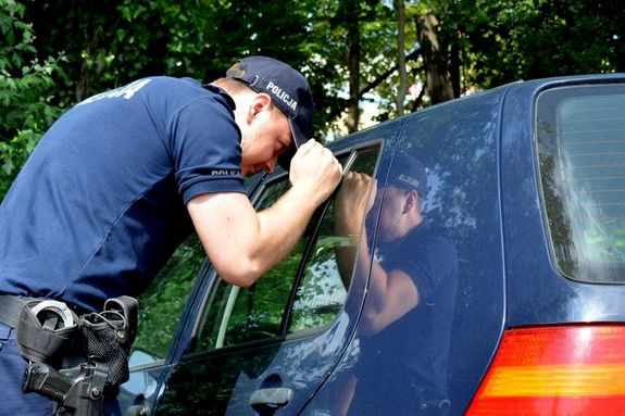Umundurowany policjant zagląda przez szybę do wnętrza samochodu