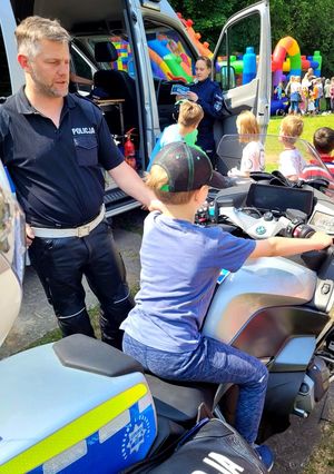 Na zdjęciu stoisko policyjne, gdzie umundurowani policjanci pokazują dzieciom oznakowany motocykl i radiowóz
