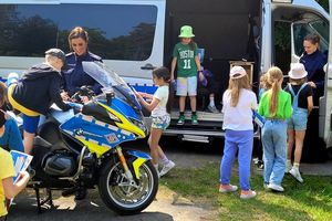 Na zdjęciu stoisko policyjne, gdzie umundurowani policjanci pokazują dzieciom oznakowany motocykl i radiowóz