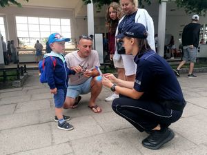 Na zdjęciu policjantka z dwiema kobietami, mężczyzną i małym dzieckiem. W tle inne osoby