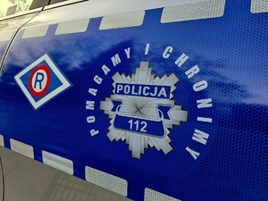 Na zdjęciu bok oznakowanego radiowozu, na którym widoczne jest logo ruchu drogowego oraz policyjna gwiazda z napisami POLICJA, 112 oraz POMAGAMY I CHRONIMY.