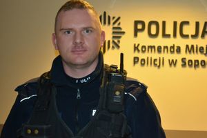 Na zdjęciu policjant, a za nim na ścianie napis POLICJA i KOMENDA MIEJSKA POLICJI W SOPOCIE