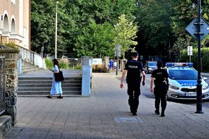 Na zdjęciu dwoje policjantów, którzy idą w stronę radiowozu. Obok nich idzie kobieta