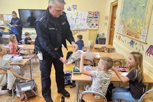 Na zdjęciu policjant, który wręcza dzieciom odblaski. W tle widoczna policjantka.