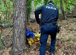 Na zdjęciu policjant, który podchodzi do leżącego w lesie mężczyzny.