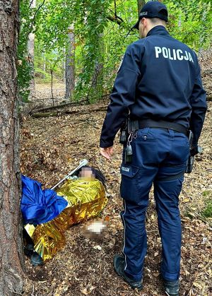 Na zdjęciu policjant i leżący w lesie mężczyzna.