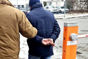 Na zdjęciu zatrzymany mężczyzna, który ma założone kajdanki na ręce trzymane z tyłu. Prowadzi go policjant w stroju cywilnym