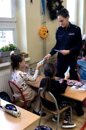 Na zdjęciu policjantka i dwójka dzieci. Jednemu z nich policjantka wręcza ulotkę