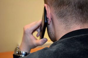 Na zdjęciu fragment sylwetki mężczyzny. Jest on tyłem i trzyma w ręku przy uchu telefon.