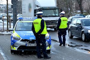 Aura zimowa. Na zdjeciu dwóch policjantów, radiowóz i jadące ulicą samochody.