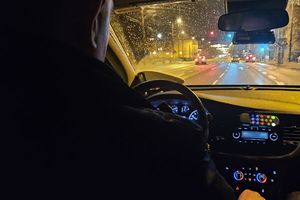 Na zdjęciu policjant we wnętrzu radiowozu, który jedzie ulicą w porze nocnej