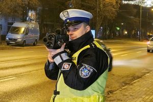 Pora nocna. Na zdjęciu policjant ruchu drogowego, który stoi przy ulicy i trzyma w ręku urządzenie do pomiaru prędkości.