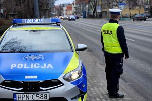 Na zdjęciu radiowóz, policjant i ulica, po której jadą samochody