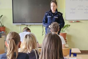 Na zdjęciu pomieszczenie klasowe, gdzie policjantka rozmawia z uczniami siedzącymi w ławkach
