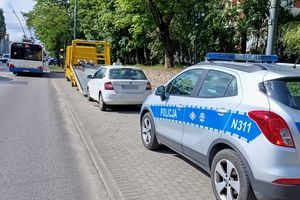 Na zdjęciu radiowóz, pojazd osobowy i pojazd laweta. Z lewej strony znajduje się ulica, po której jedzie autobus