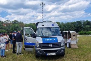 Na zdjęciu radiowóz, przy którym stoi policjantka i inne osoby