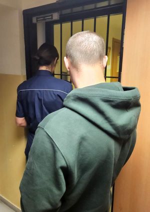 Na zdjęciu zatrzymany mężczyzna i policjantka, która wchodzi do pomieszczenia