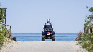 Na zdjęciu policjant na quadzie, który znajduje się przy wejściu na plażę. Za nim w tle woda