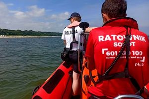 Na zdjęciu policjant i ratownik wodny, którzy płyną łodzią w okolicy plaży