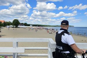 Na zdjęciu policjant, który patrzy na ludzi wypoczywających na plaży.