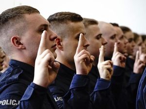 Na zdjęciu grupa policjantów, którzy stoją w rzędzie, mają podniesioną dłoń i składają przysięgę