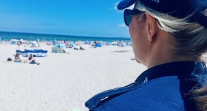 Na zdjęciu policjantka, a za nią plaża i ludzie, którzy na niej wypoczywają