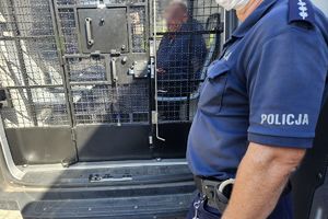 Na zdjęciu policjant i zatrzymany mężczyzna siedzący w samochodzie w pomieszczeniu dla osób zatrzymanych