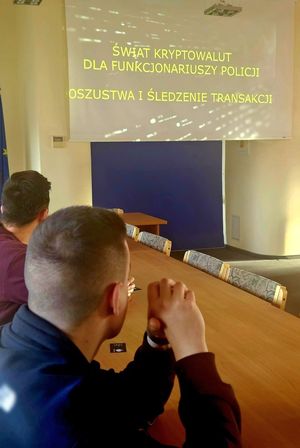 Na zdjęciu pomieszczenie służbowe i policjanci w strojach cywilnych, którzy patrzą w stronę wyświetlanej prezentacji multimedialnej