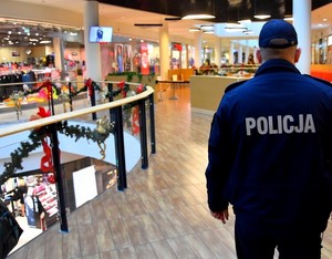 Na zdjęciu policjant idący przez hol galerii sklepowej, która przystrojona jest w stylu świątecznym