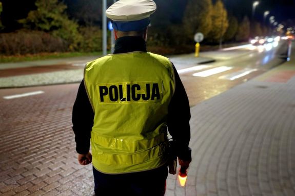 Na zdjęciu policjantka ruchu drogowego, która stoi przy ulicy i patrzy w stronę jadących ulicą samochodów