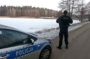 Na zdjęciu policjant, radiowóz i zamarznięty zbiornik, na którym leży śnieg