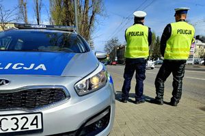 Na zdjęciu radiowóz i dwóch policjantów stojących przy ulicy